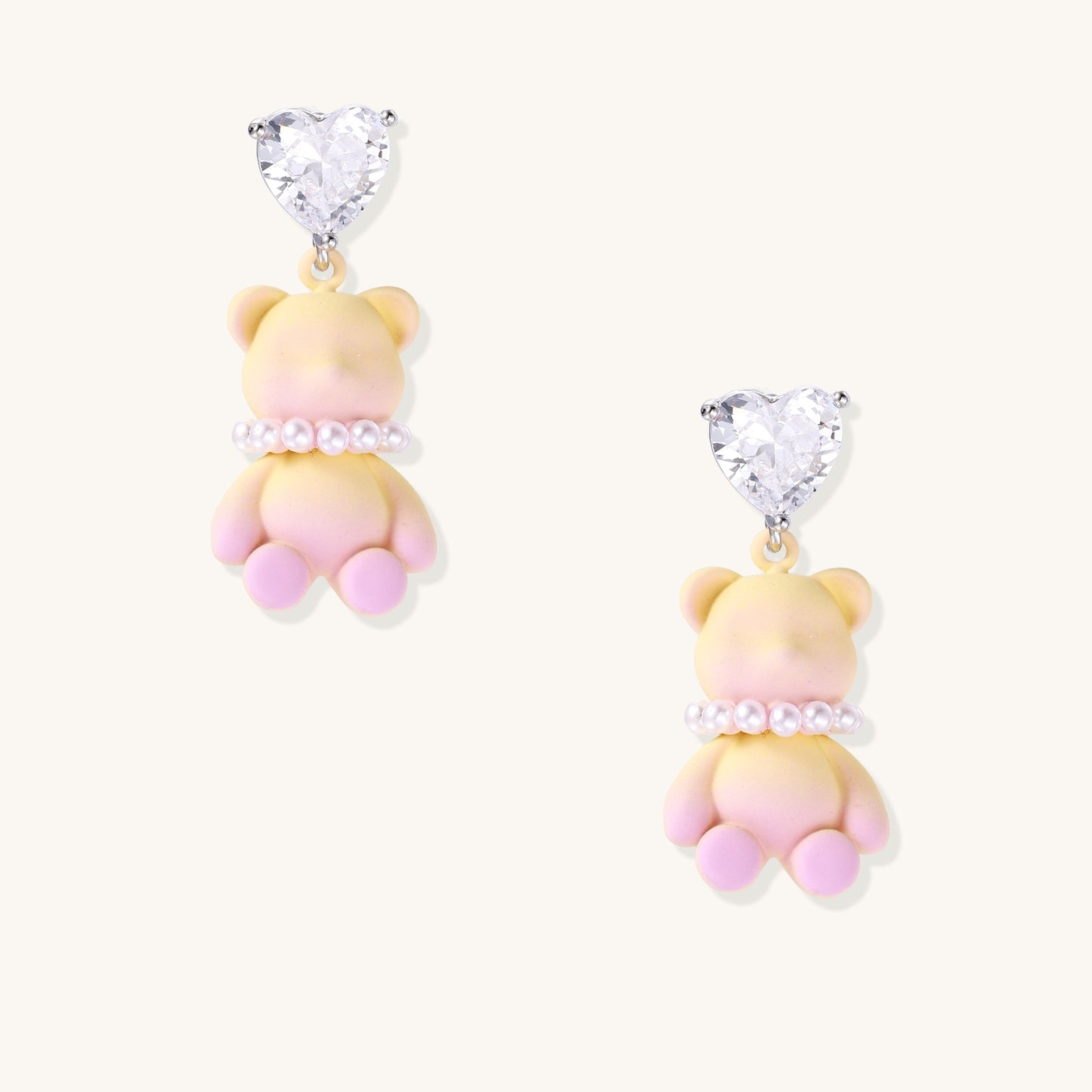 Cute teddy bear earrings with heart-shaped crystals, gold plating, and white pearl accents in pink and blue variants