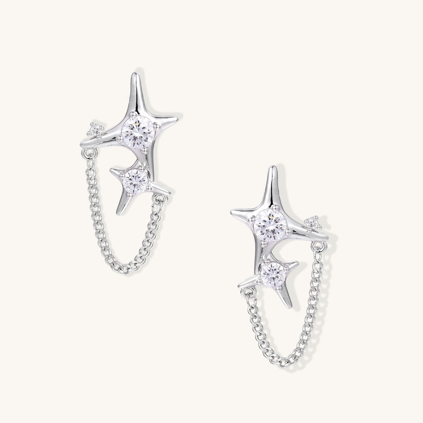 Delicate gold-plated star earrings with sparkling zirconia crystals connected by fine chains on cream background.