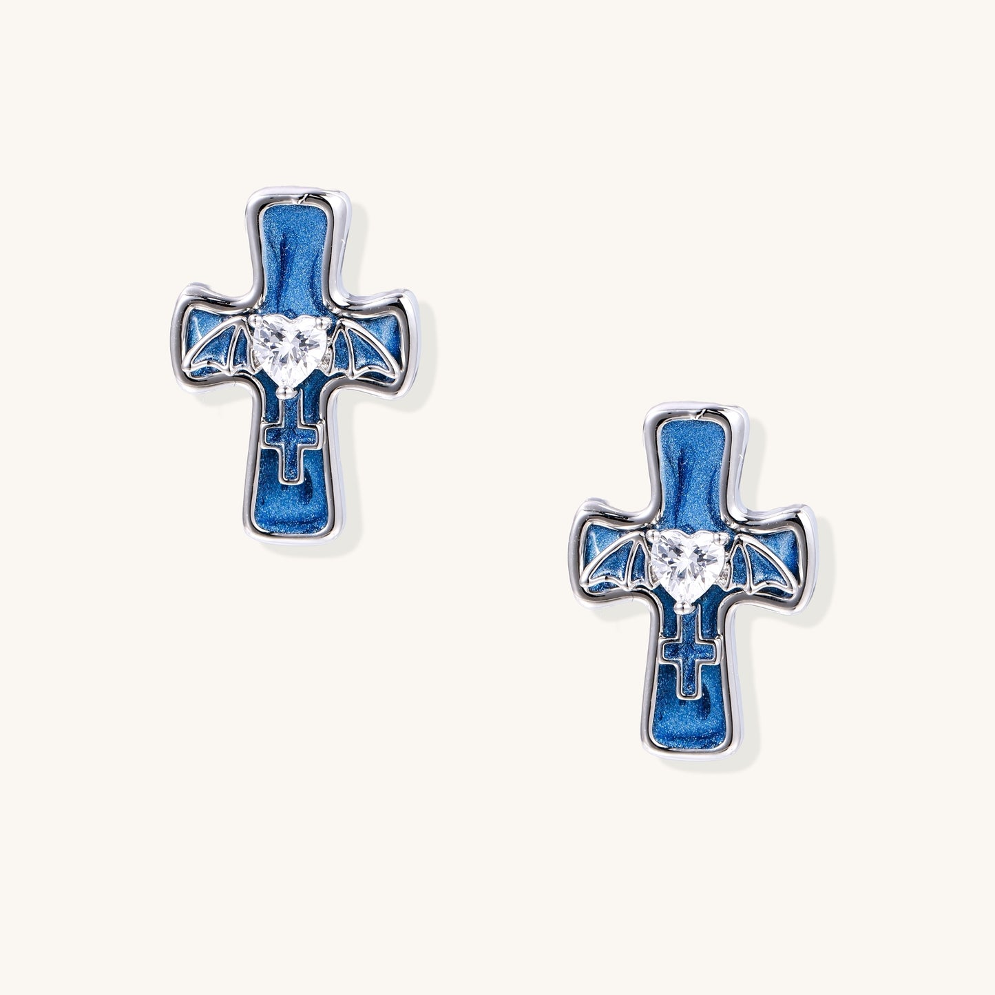 Blue enamel cross stud earrings with gold plating, clear zirconia center stones, and bat wing details on white background.