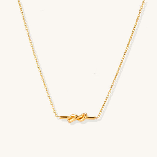 Dainty 18K gold plated stainless steel chain necklace with minimalist knot pendant on cream background.