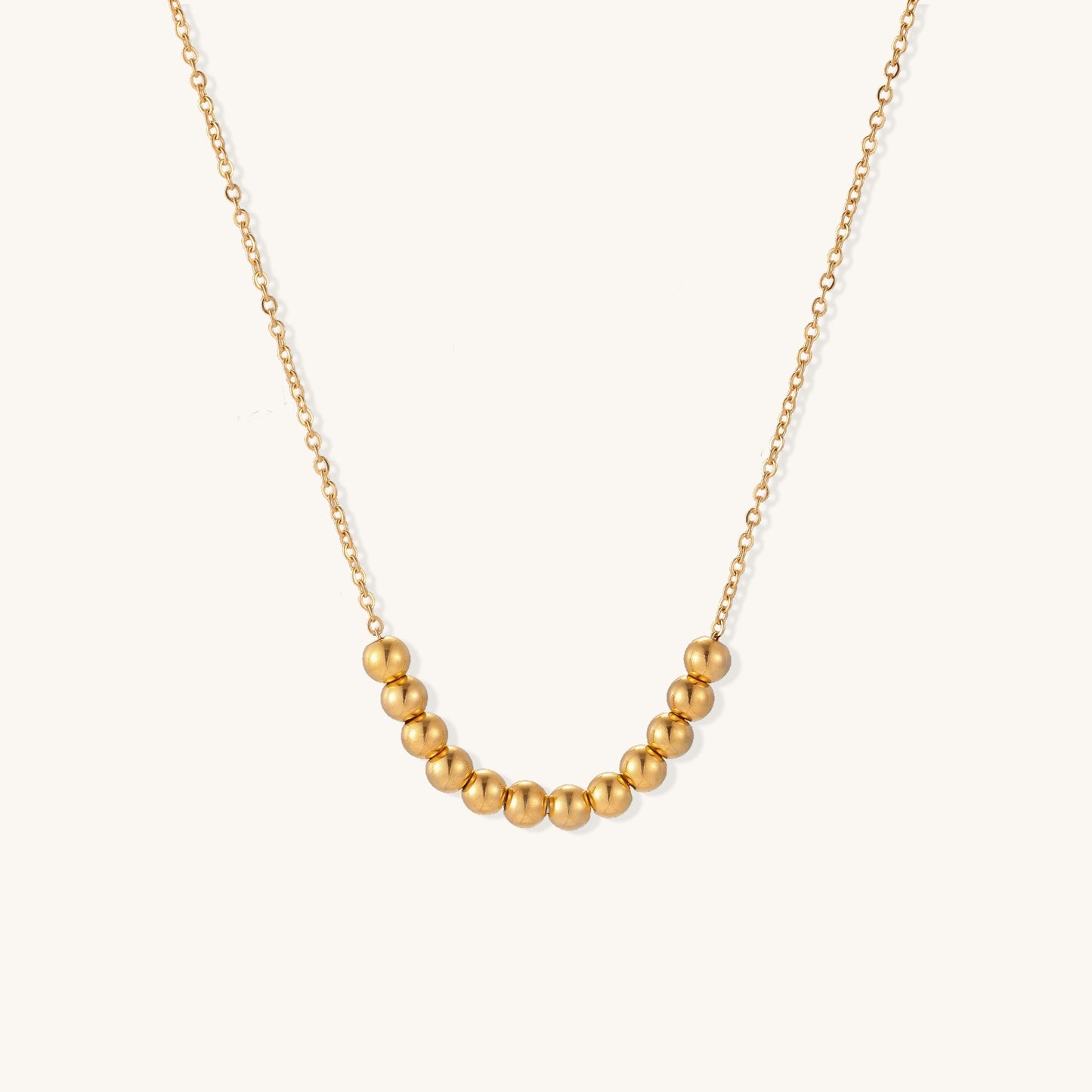 Delicate gold-plated chain necklace featuring clustered spherical beads arranged in elegant curve against white background.