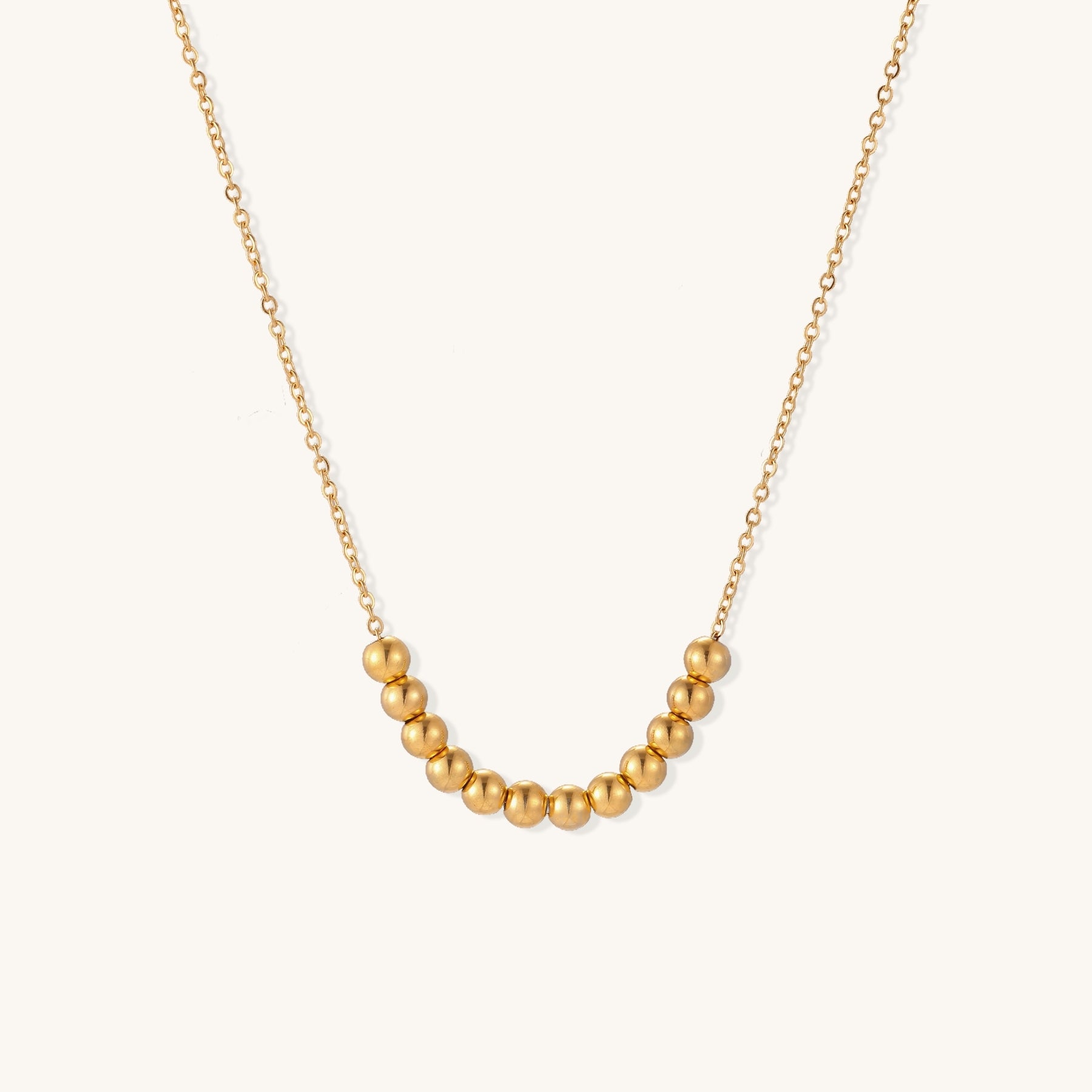 Delicate gold-plated chain necklace featuring clustered spherical beads arranged in elegant curve against white background.