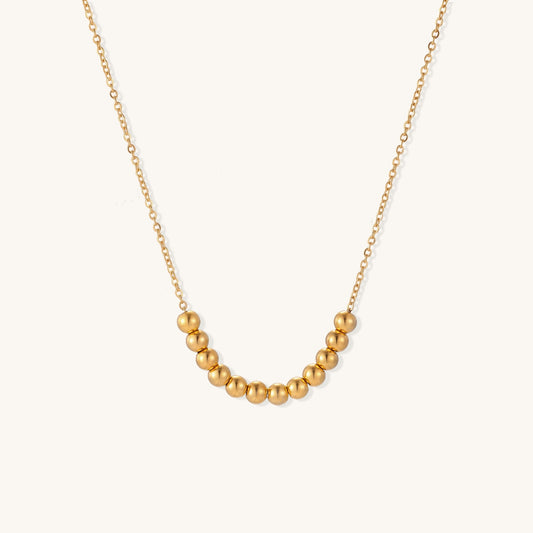 Delicate gold-plated chain necklace featuring clustered spherical beads arranged in elegant curve against white background.