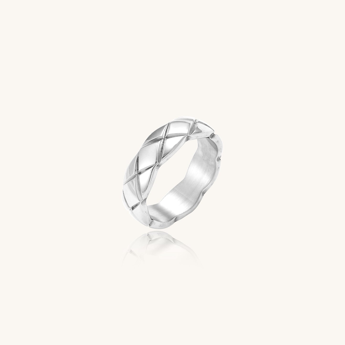 Close-up of a polished stainless steel ring featuring a geometric quilted diamond pattern on white background.