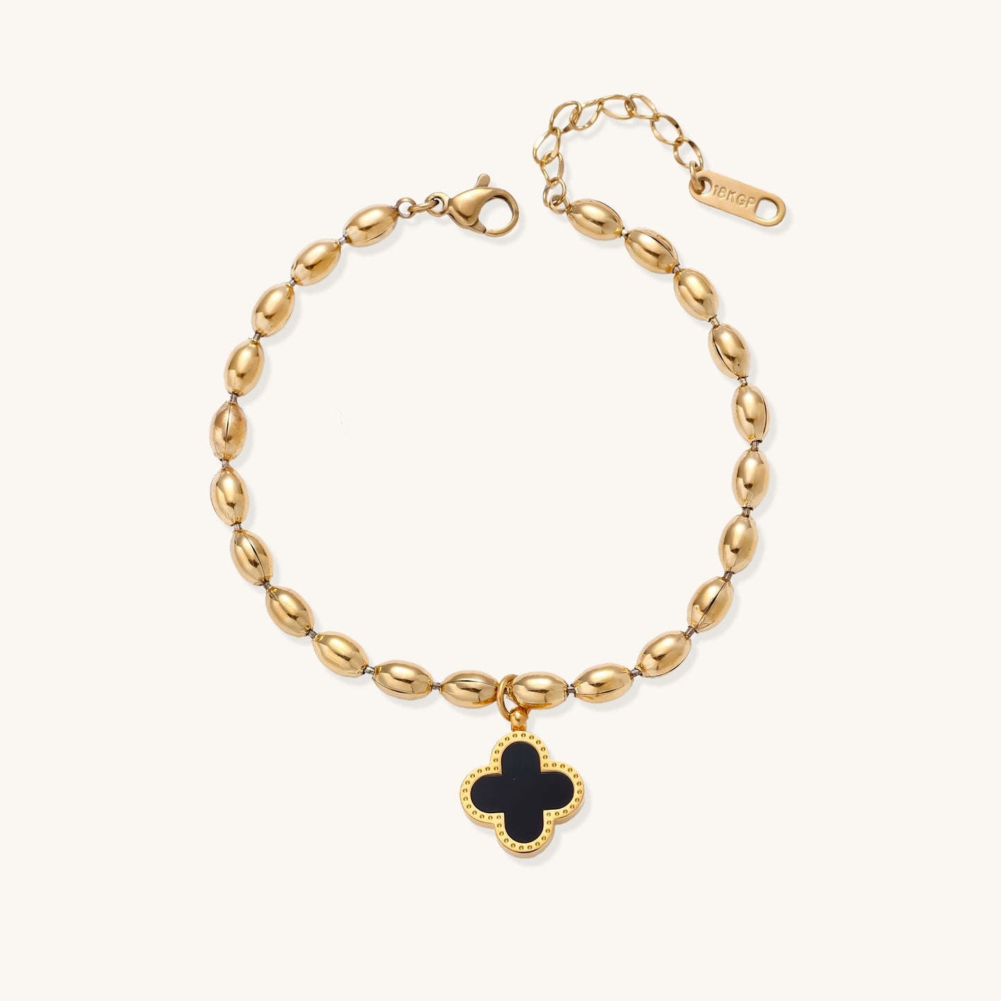 Dainty gold-plated beaded bracelet with oval links and four-leaf clover charm pendant on neutral background.