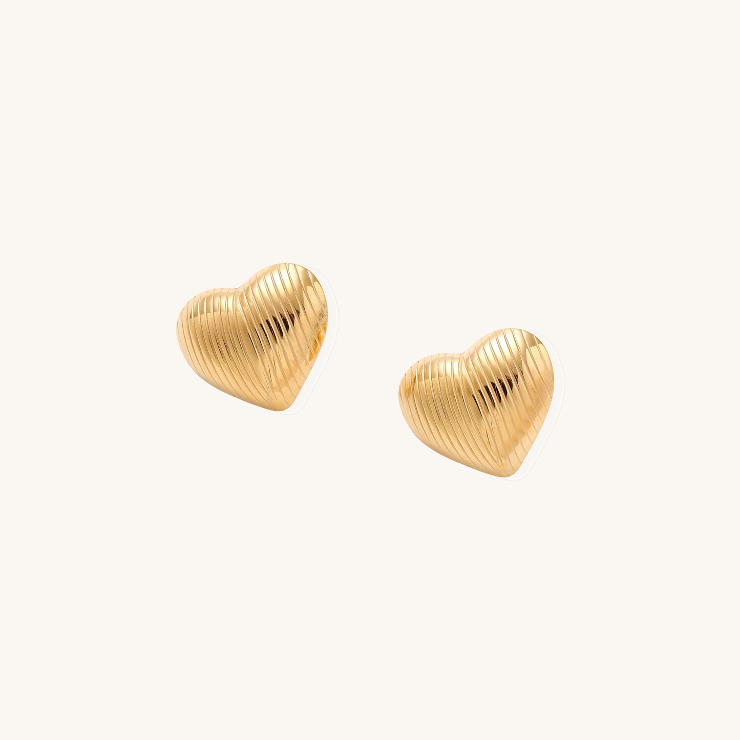 Close-up of ridged heart-shaped gold-plated stud earrings with textured surface pattern on cream background.
