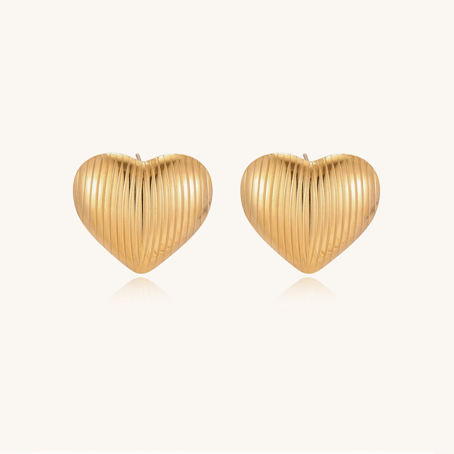 Close-up of ridged heart-shaped gold-plated stud earrings with textured surface pattern on cream background.