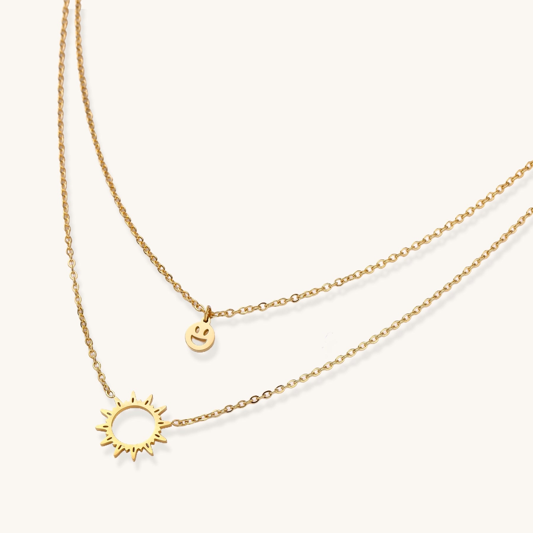 Delicate gold-plated layered necklace with smiley face and sun pendants on white background, showing adjustable chain.