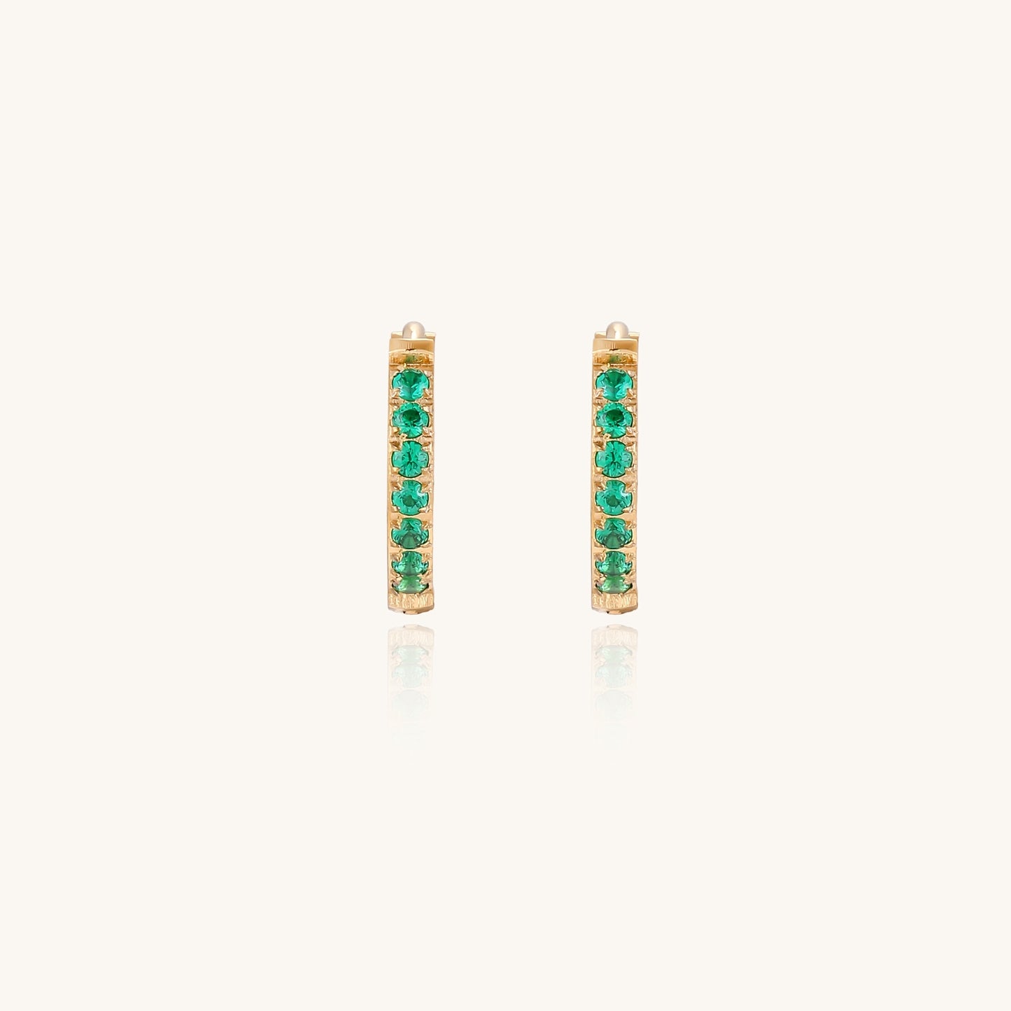 Small gold-plated huggie hoop earrings with emerald green cubic zirconia stones, one open showing hinge mechanism