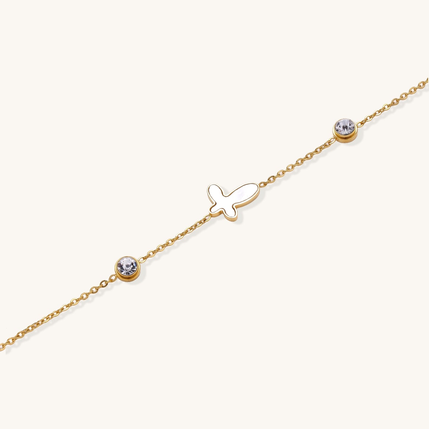 Delicate gold-plated bracelet featuring white mother-of-pearl cross charm and crystal accents on white background.